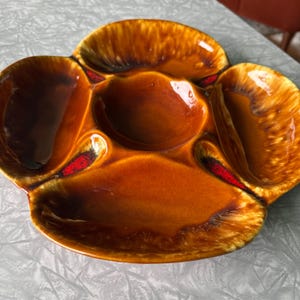 May include: A brown ceramic serving dish with four individual sections and a central dip. The dish has a mottled glaze with red accents.