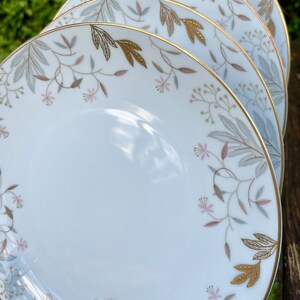 May include: Set of four white ceramic plates with a gold rim and a delicate floral design in shades of gray, pink, and gold.