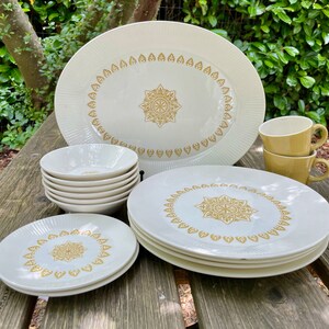 May include: A set of white ceramic dinnerware with a gold floral pattern. The set includes a large oval platter, four salad plates, four bowls, and two mugs.