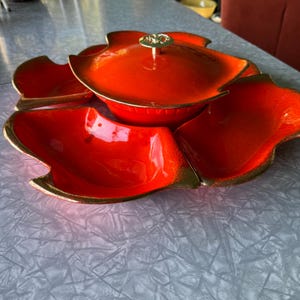 May include: A set of four orange ceramic serving dishes with gold trim. The dishes are arranged in a flower shape with a central bowl with a lid.