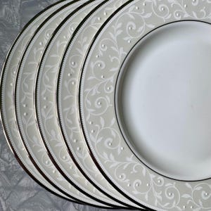 May include: Set of six white dinner plates with a silver rim and a delicate gray floral pattern.