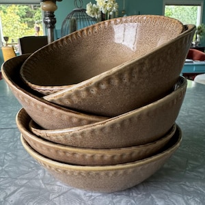 May include: A stack of four brown ceramic bowls. The bowls have a textured surface and a slightly irregular shape. The rims of the bowls are decorated with a series of small, raised dots. The bowls are stacked on top of each other.
