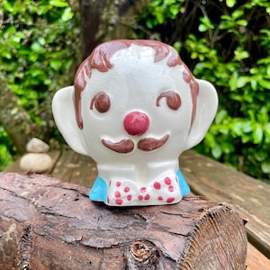 May include: A ceramic figurine of a person with brown hair, a white face, a red nose, a brown moustache, and a blue and white polka dot bow tie.