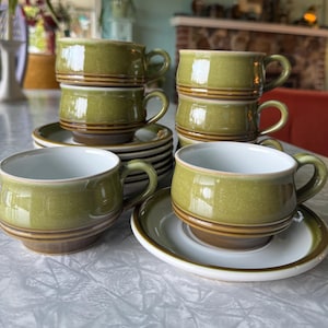 May include: Set of six green and brown ceramic teacups and saucers. The cups and saucers have a speckled glaze and a brown band around the rim.