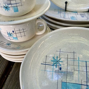 Puede incluir: Juego de vajilla de cerámica vintage con un patrón geométrico en tonos de azul, gris y blanco sobre un fondo crema.