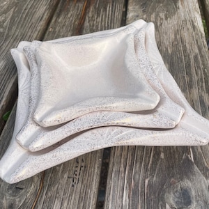 May include: Three white ceramic dishes with a textured surface. The dishes are stacked on top of each other, with the largest dish on the bottom and the smallest dish on top.