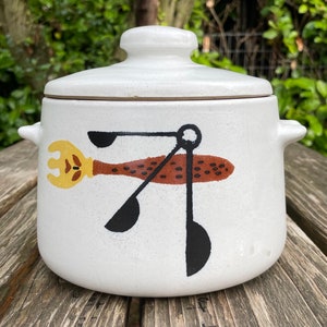 May include: White ceramic crock pot with a lid. The crock pot has a black and brown design of a stylized bird with a long beak and a set of three black spoons.