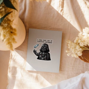 May include: A white card with a black and white illustration of Darth Vader holding a water bottle. The text on the card reads "I find your lack of hydration disturbing."