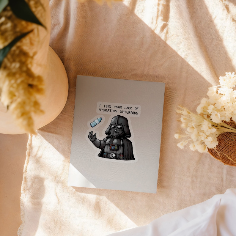 May include: A white card with a black and white illustration of Darth Vader holding a water bottle. The text on the card reads "I find your lack of hydration disturbing."