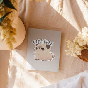 May include: A gray card with the text "PUG LIFE" printed in black. A cartoon pug with brown eyes and a black nose is printed below the text.