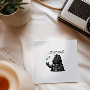 May include: A white card with a black and white illustration of Darth Vader holding a water bottle. The text on the card reads "I find your lack of hydration disturbing."