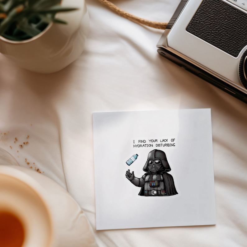 May include: A white card with a black and white illustration of Darth Vader holding a water bottle. The text on the card reads "I find your lack of hydration disturbing."