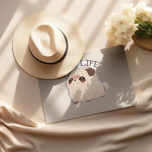 May include: A beige and brown pug cartoon sticker with the text "Good Life" on a white background. The sticker is on a beige surface with a straw hat.