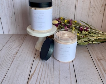 May include: Two jars of whipped body butter with black lids. The jars are labeled "Wild Child Studio Co." and "Peach Blossom" in white text. The jars are on a white wooden surface with dried flowers in the background.