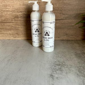 May include: Two clear plastic lotion bottles with white pump dispensers. The bottles are labelled "Brown Sugar & Fig" and "Wild Child Studio Co." The lotion inside is white. Each bottle contains 118 ml.