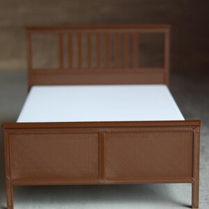 May include: A brown wooden bed frame with a white mattress. The headboard has a slatted design, and the footboard is solid. The bed is a miniature model, likely for a dollhouse or display.
