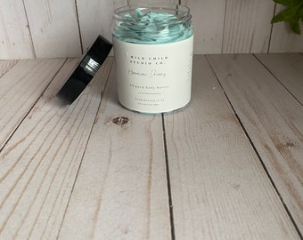 May include: A white jar with a teal lid filled with a light blue whipped body butter. The jar has a label that reads "Wild Child Studio Co. - Hawaiian Dreams Whipped Body Butter Handmade in PA"