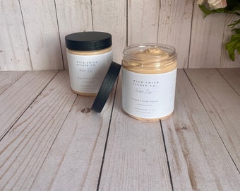May include: Two white jars of whipped body butter with black lids. The jars are labeled "Wild Child Studio Co." and "Harbor Rose" in black text. The jars are sitting on a light wood surface.