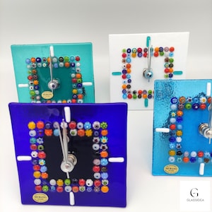 Può includere: Quattro orologi quadrati in vetro con bordi in mosaico di vetro colorato. Gli orologi sono in blu, turchese, bianco e azzurro. Ogni orologio ha un quadrante nero con lancette bianche e una piccola etichetta che dice "Murano Glass Made in Italy".