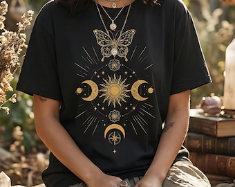 以下が含まれることがあります： 金色の蝶と天体のデザインが施された黒いTシャツ。グラフィックには太陽、三日月、星が含まれています。シャツは半袖で、丸いネックラインです。デザインはシャツの前面の中央に配置されています。