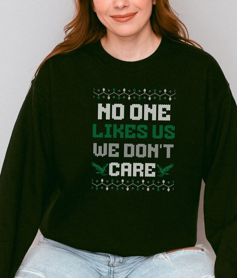 Peut inclure: Sweat-shirt noir avec l'inscription "NO ONE LIKES US WE DON'T CARE" en blanc et vert. Le motif comprend des &eacute;l&eacute;ments d&eacute;coratifs et deux graphiques d'aigles verts. V&ecirc;tement d&eacute;contract&eacute;.
