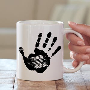 May include: White ceramic coffee mug with a black handprint design. The handprint is made up of tire tread patterns.