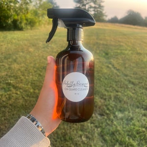 May include: A brown glass spray bottle with a black trigger sprayer. The bottle has a white label with the text "Perfectly Pampered by Maddi ON GUARD CLEANER 20 oz."