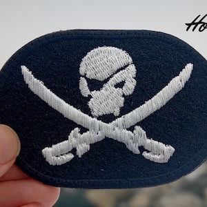 Op de afbeelding: Wit geborduurde piraten schedel en gekruiste botten patch op een zwarte achtergrond.