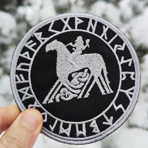 May include: Black and white embroidered patch with a circular design. The centre features a white horse with a rider, surrounded by a circle of white runes. The runes are in a circular pattern around the horse and rider.
