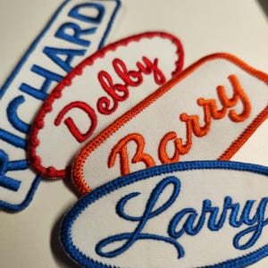 May include: Four white fabric patches with embroidered names in different colors. The names are "Richard", "Debby", "Barry", and "Larry".