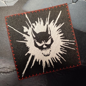 Peut inclure: Patch brodé noir avec un crâne blanc et des crocs avec un motif blanc en pointe autour.