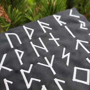 May include: Black fabric with white embroidered runes. The runes are arranged in a random pattern.