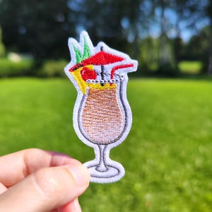 May include: Embroidered iron-on patch of a tropical cocktail with a red umbrella, pineapple, and a straw. The cocktail is in a tall glass with a white outline.