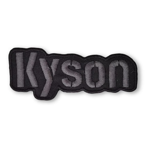 Op de afbeelding: Zwarte geborduurde patch met het woord "Kyson" in grijze letters.