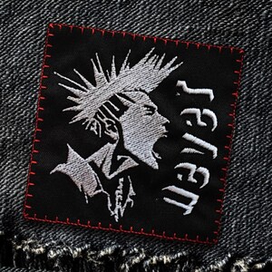 Può includere: Toppa ricamata in bianco e nero con una figura in stile punk rock con un mohawk e la parola "JAIL" scritta verticalmente in bianco.