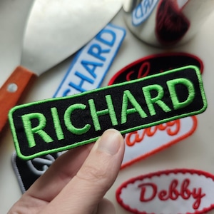 Op de afbeelding: Een zwart en groen geborduurd patch met de naam "RICHARD" in groene letters.