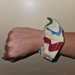 Puede incluir: Un scrunchie de tela blanca con patrones abstractos rojos, azules, verdes y amarillos.