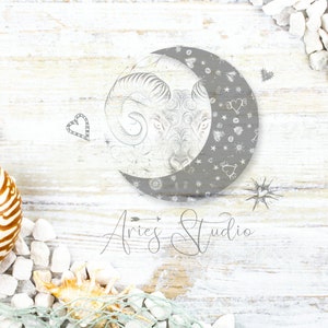 Könnte beinhalten: Eine kreisförmige Grafik mit einem grauen Halbmond und einer Widderkopf-Illustration, umgeben von kleinen Stern- und Herzsymbolen. Unter der Grafik steht der Text Aries Studio in einer Schreibschrift auf einem weißen Holzuntergrund.