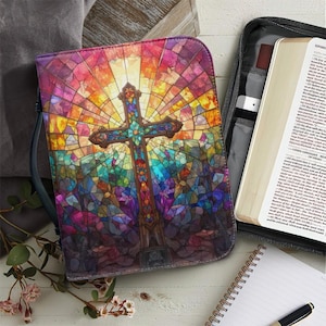 May include: A Bible cover with a stained-glass design featuring a cross. The cover is predominantly purple, blue, and orange, with a detailed cross at the center. A Bible and other accessories are visible nearby.