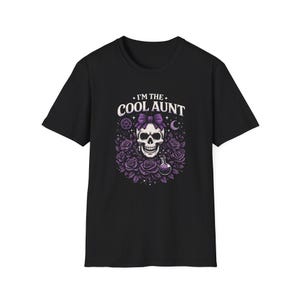 May include: Black t-shirt featuring a skull with a purple bow, surrounded by purple roses. The text "I'M THE COOL AUNT" is above the skull. A pentagram, moon, and potion bottle are also in the design.