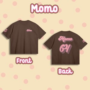 K&ouml;nnte beinhalten: Ein braunes T-Shirt mit rosa Schrift auf Vorder- und R&uuml;ckseite. Die Vorderseite zeigt "Twice" und die R&uuml;ckseite "Momo 62".