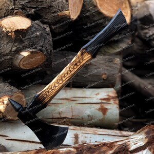 Pu&ograve; includere: Un'ascia nera con manico in legno. Il manico &egrave; decorato con un motivo geometrico e ha una macchia marrone scuro. L'ascia &egrave; appoggiata su una pila di tronchi.