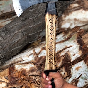 Pu&ograve; includere: Un'ascia da mano nera e argentata con un manico in legno. Il manico &egrave; intagliato con un motivo e bruciato con una finitura marrone scuro. La testa dell'ascia &egrave; affilata e ha una leggera curva sulla lama.