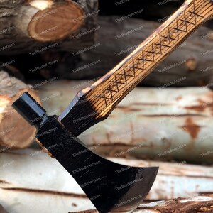Pu&ograve; includere: Un'ascia artigianale nera e marrone con manico in legno. Il manico ha un design intagliato ed &egrave; appoggiato su una pila di tronchi.