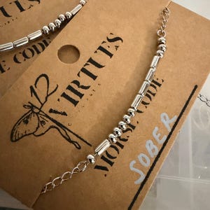 May include: A white ceramic mug with a black handle and the text "But First, Coffee" in a bold, black font. The mug is set against a blurred background, suggesting a cozy setting.