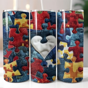 May include: Three stainless steel insulated tumblers with a puzzle piece design. The design features a variety of colorful puzzle pieces in red, yellow, blue, and orange, with a white heart-shaped puzzle piece in the center. Each tumbler has a clear straw.