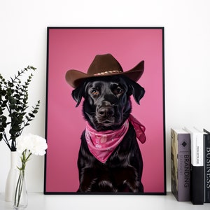 K&ouml;nnte beinhalten: Ein schwarzer Labrador Retriever mit einem braunen Cowboyhut und einem rosafarbenen Bandana vor einem rosafarbenen Hintergrund.