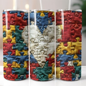 May include: A set of three stainless steel tumblers with a colorful jigsaw puzzle design. The puzzle pieces are in shades of red, yellow, blue, and green, with a white heart-shaped puzzle in the center. Each tumbler has a clear lid and a white straw.