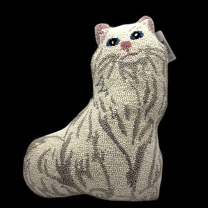 May include: A decorative throw pillow shaped like a sitting cat, crafted with a textured hooked yarn finish. The cat features a cream-colored base with grey striped patterns, blue eyes, a pink nose, and pink-tinted inner ears, with a small tag attached.