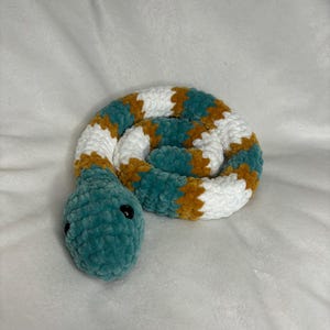 May include: A crocheted snake toy with a teal green body, white and brown stripes, and black eyes.
